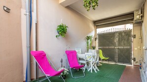 Een klein terras met twee roze stoelen, een tafel met een witte tafelkleed en hangende planten.