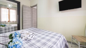 Een slaapkamer met een bed, een televisie, een spiegel en een houten stoel.