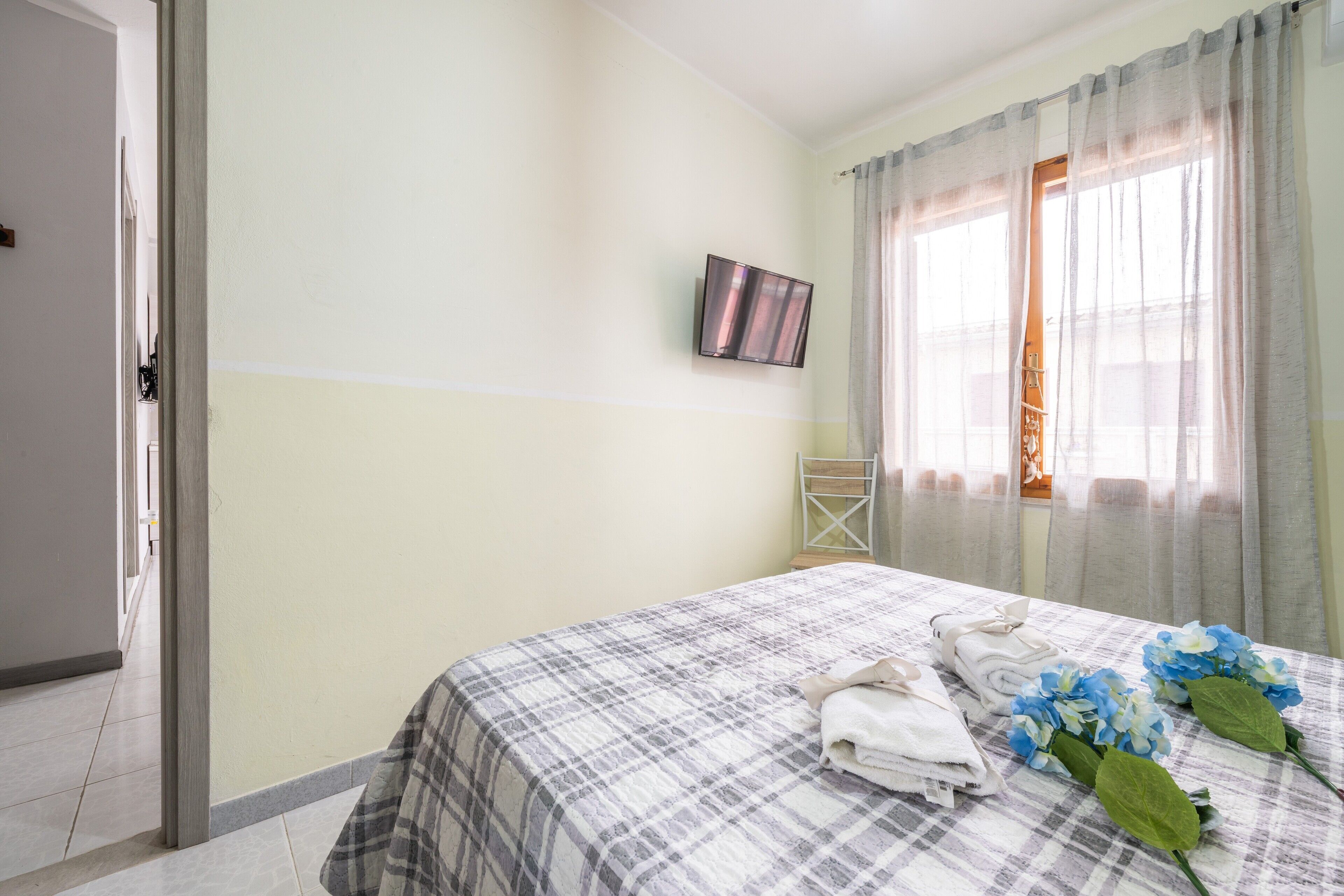 A hotel room with a bed, a television, and a window with curtains.