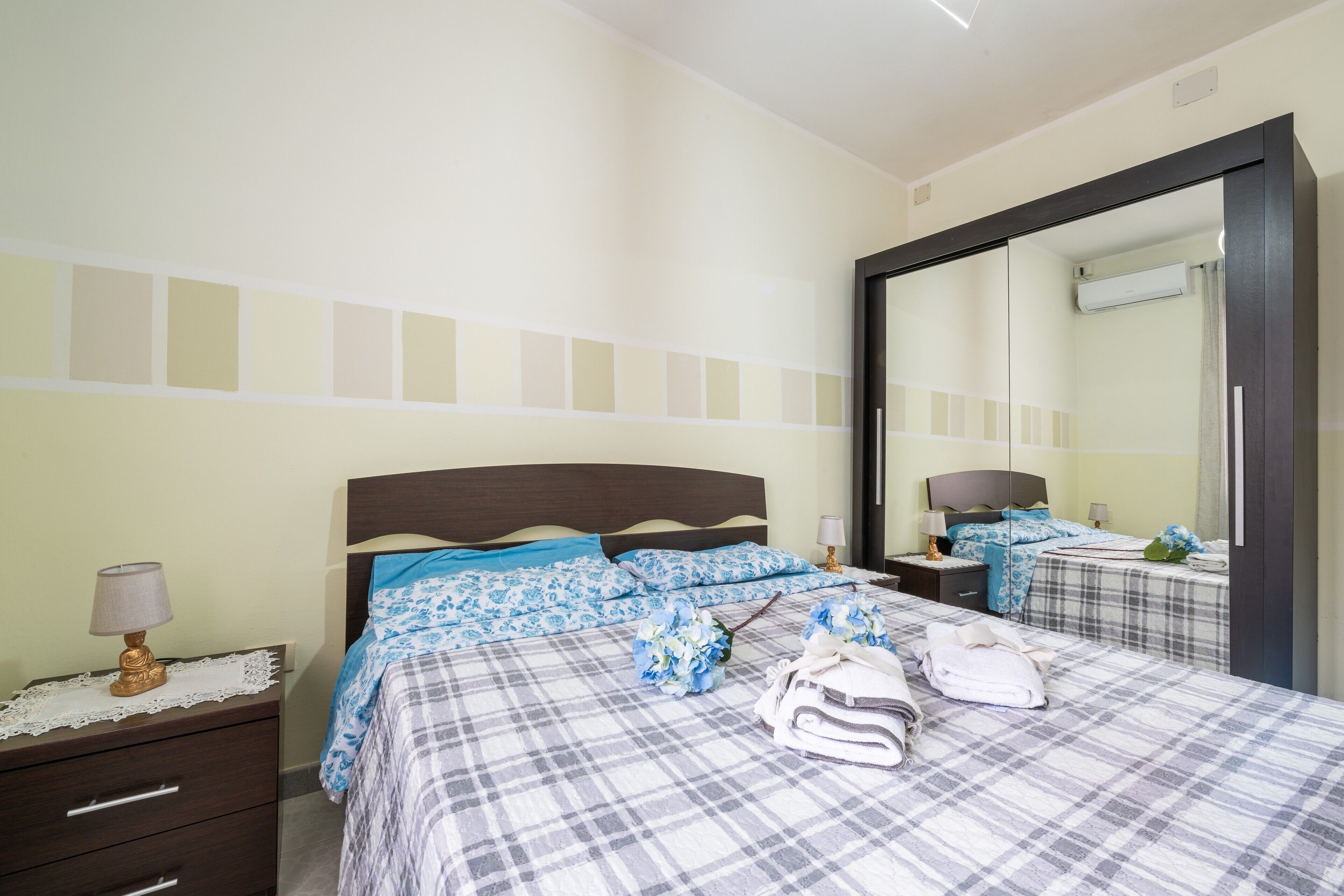 Une chambre à coucher comprenant un lit, une table de chevet, une commode, un miroir et un mur avec un interrupteur.