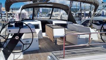 Das Deck einer Yacht mit Steuerpult, gepolsterten Sitzgelegenheiten und einem überdachten Bereich.