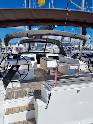 A yacht's deck with a steering wheel, a cushioned seating area, and a covered section.