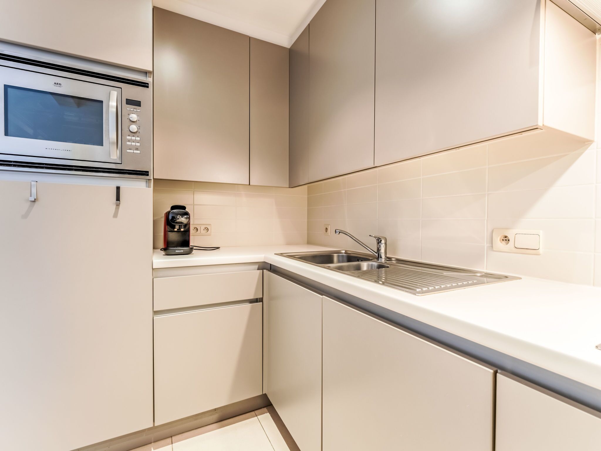 Eine moderne Küche mit Einbau-Mikrowelle, einer Kaffeemaschine und einer Spüle aus Edelstahl.