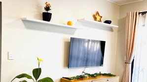 Een woonkamer met een aan de muur bevestigde televisie, een houten kast, een potplant en een kleine tafel.