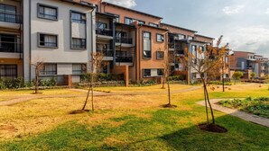 Een rij moderne appartementencomplexen met balkons, een gazon en een heldere lucht.