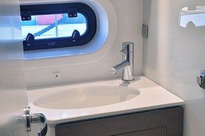 Un baño con lavamanos blanco, grifo cromado y ventana con vista a un estacionamiento.