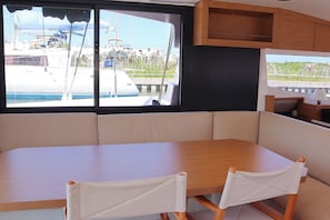 Um interior moderno com uma mesa de madeira e assentos acolchoados, grandes janelas com vista para um porto e armários embutidos de madeira.