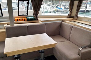 A corner seating area with a table, a window with curtains, and a view of boats. - Sun-Kissed Sailing Adventure in Isla de Mahe, Seychelles (Victoria)