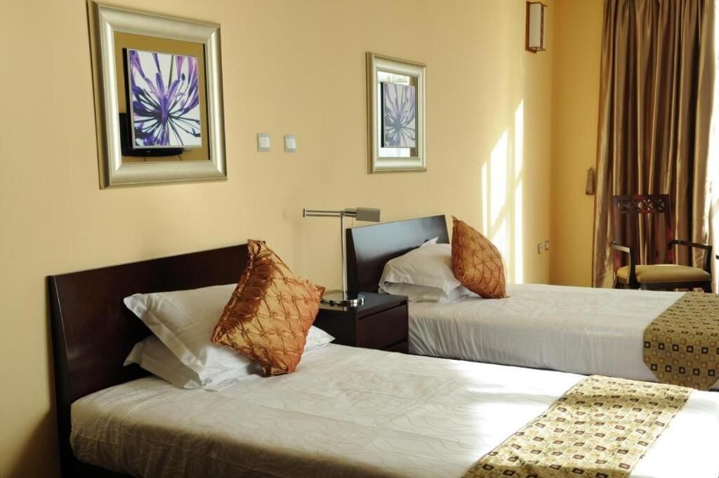 A hotel room with two beds, a desk, a chair, and artwork on the walls.