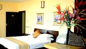 A hotel room with a bed, a nightstand, a vase with flowers, and two framed pictures on the wall. - Destiny Addis Hotel (Addis Ababa)
