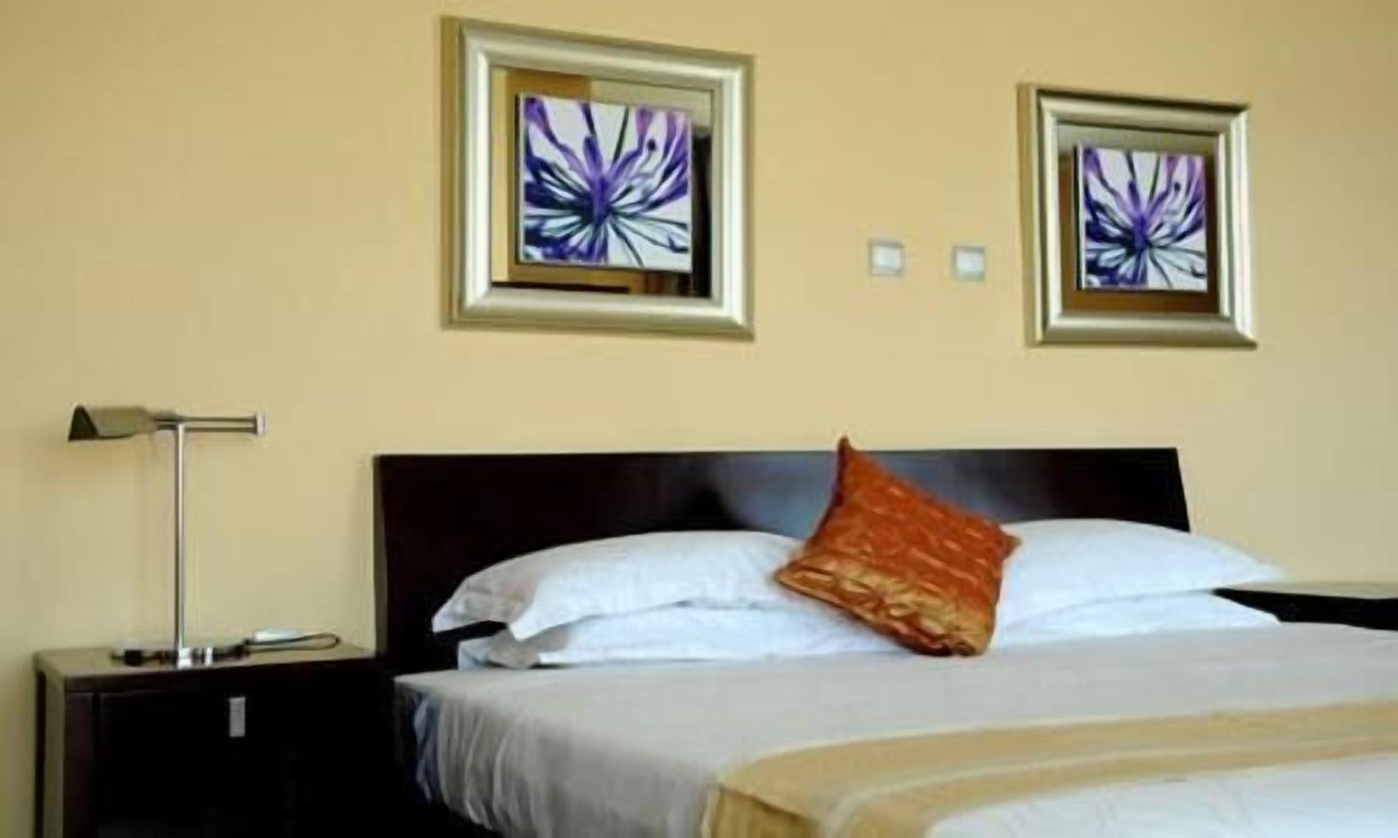 Ein Hotelzimmer mit einem Bett, zwei gerahmten abstrakten Bildern, einem Nachttisch und einer Lampe.