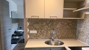 A modern kitchen with a stainless steel sink, light-colored cabinets, and a patterned backsplash. - Studio 'Arcobaleno' with Sea View Balcony, Wi-Fi and Air Conditioning (Savona)