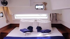 A neatly made bed with white and blue bedding, a small window with curtains, and a view of the outside. - Caribbean Dream: Sun-soaked Sailing Adventure from Tortola, Islas Vírgenes Británicas (Road Town)