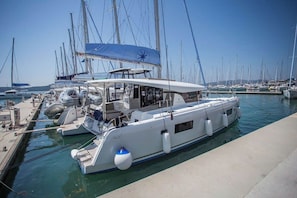 Eine Marina mit mehreren vor Anker liegenden Yachten, einem überdachten Bereich mit blauer Markise und blauem Himmel.