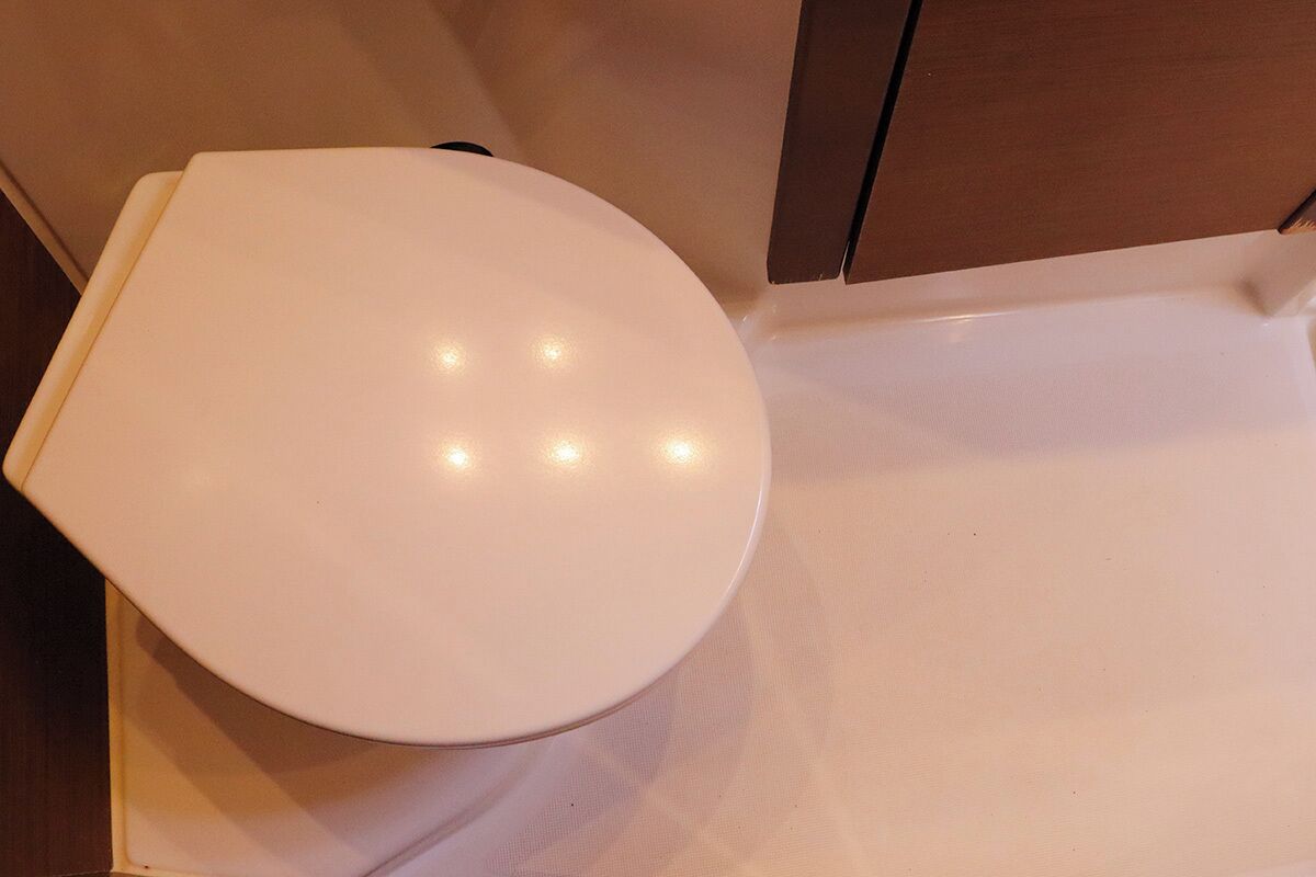 A white toilet in a bathroom with a wooden cabinet above it.