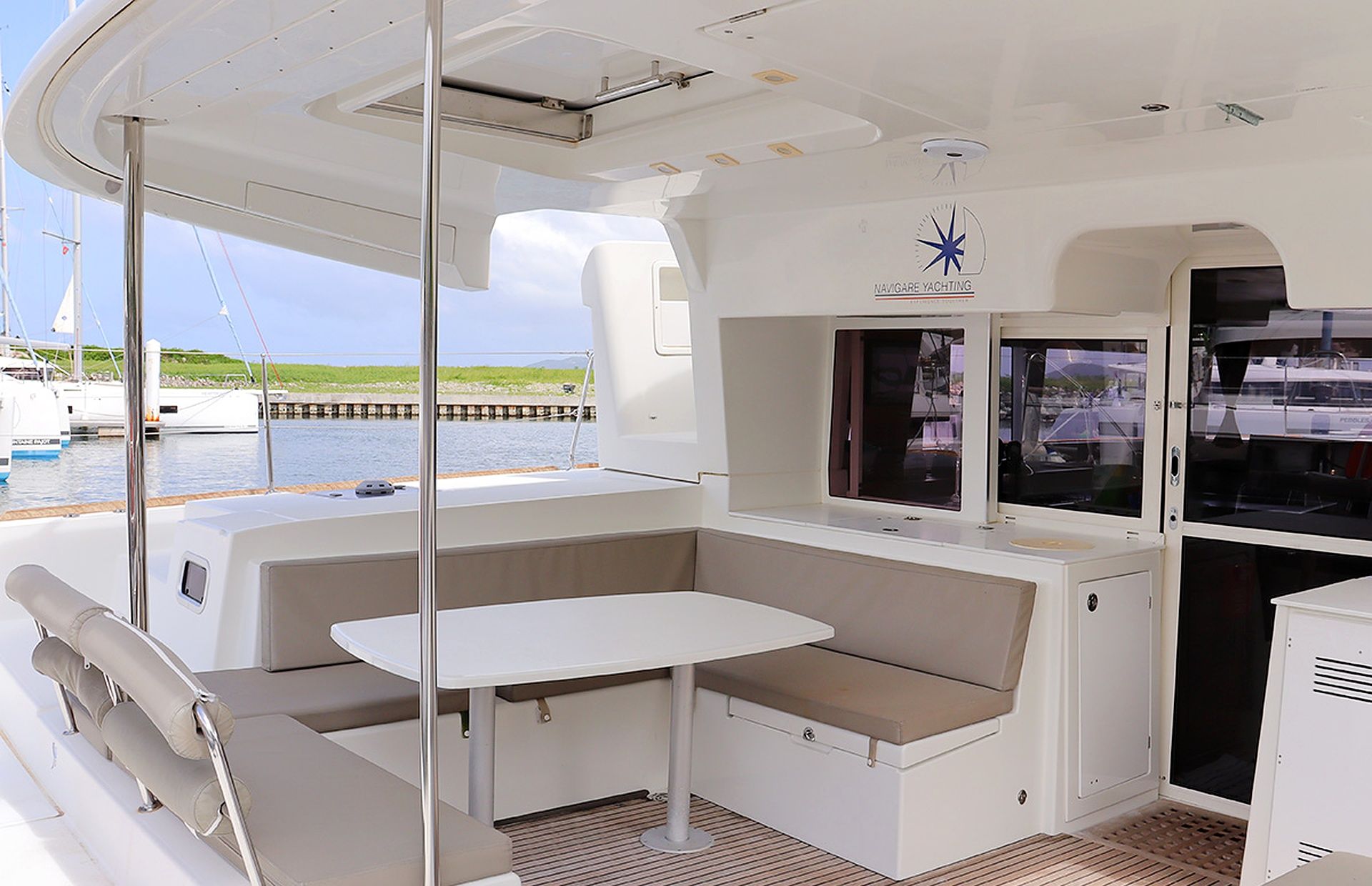 A yacht interior with a white table, cushioned seating, and a window overlooking the water.