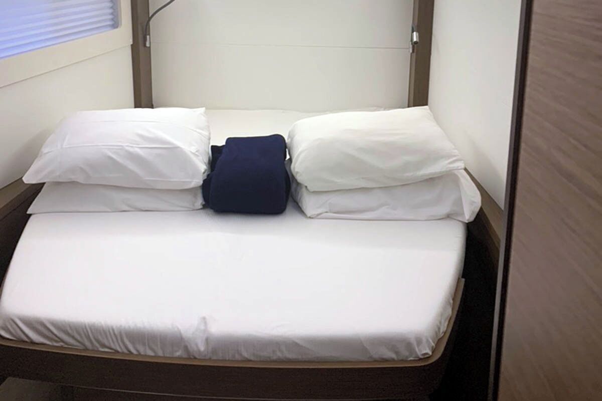 Uma cama de solteiro com roupa de cama branca e um travesseiro escuro no centro.