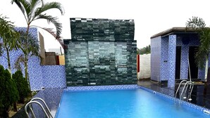 Ein Schwimmbecken mit einer gefliesten Kante, einer Steinmauer und einem kleinen Nebengebäude.