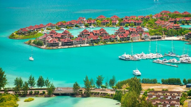 Un complex turístic a la costa amb diversos edificis, una marina plena d'iots i un mar turquesa cristal·lí.