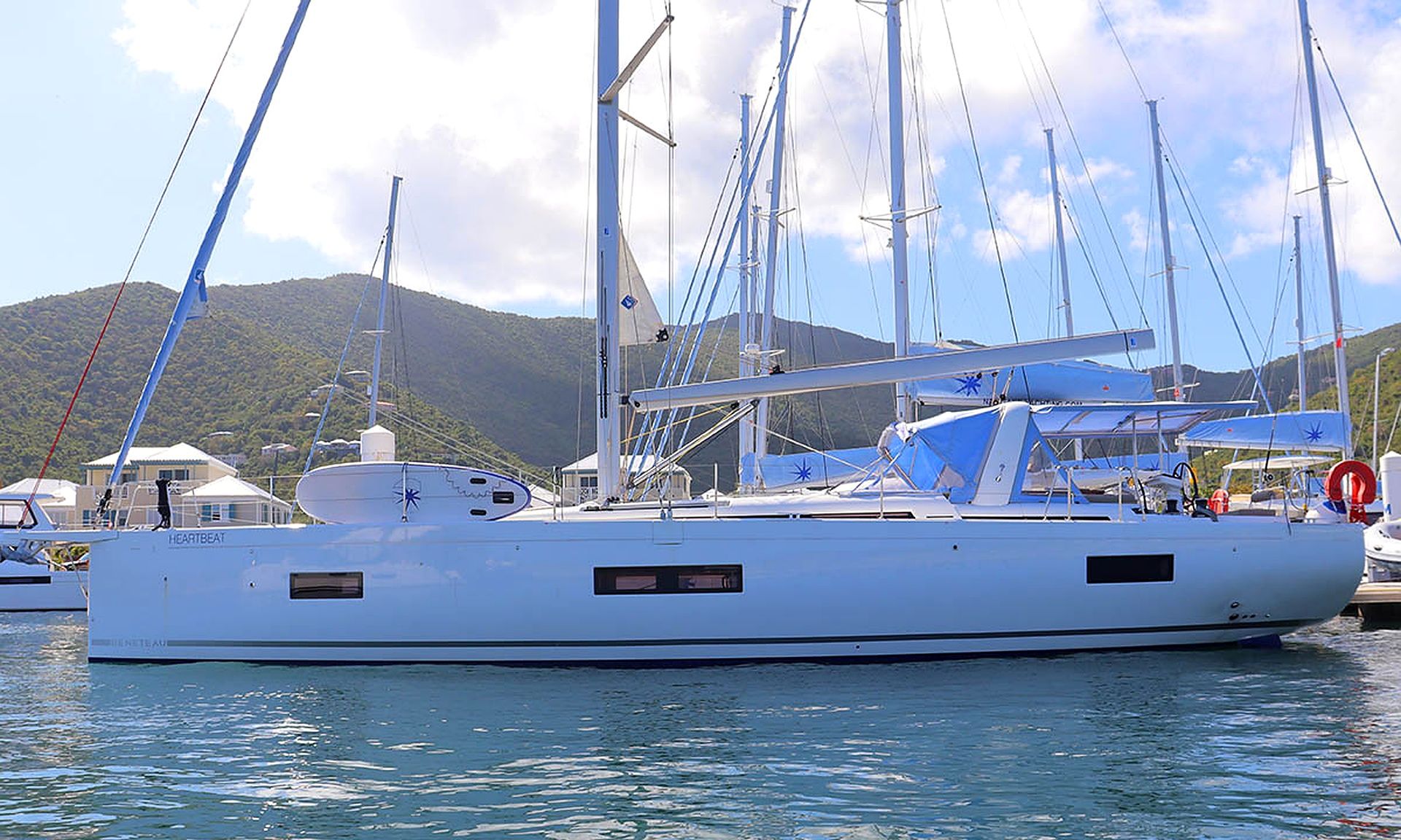 Eine große weiße Yacht liegt in einer Marina festgemacht, umgeben von ruhigem Wasser und mit Bergen im Hintergrund. Mehrere Masten und Segel sind zu sehen.