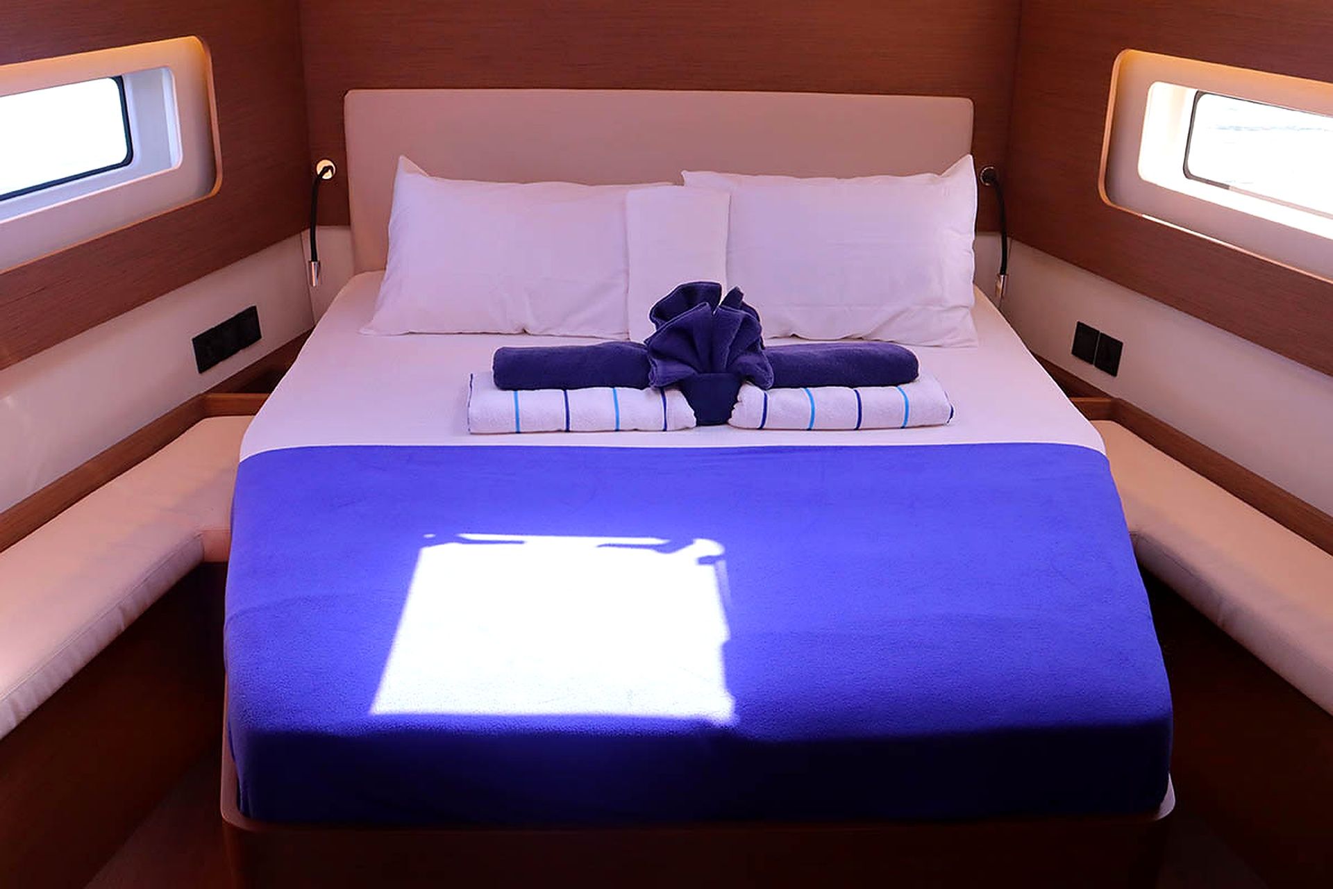 Un lit avec des draps blancs et une couverture bleue, des oreillers et une serviette pliée.