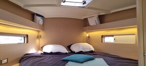 Una cabaña pequeña y luminosa con una cama, dos almohadas, una ventana y un estante con bolsas.