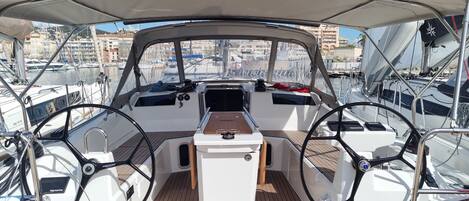 A boat's interior with a steering wheel, control panel, and wooden deck.
