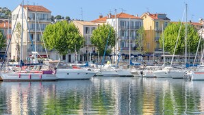 Un puerto deportivo con barcos amarrados, edificios con balcones y árboles a lo largo de la costa.