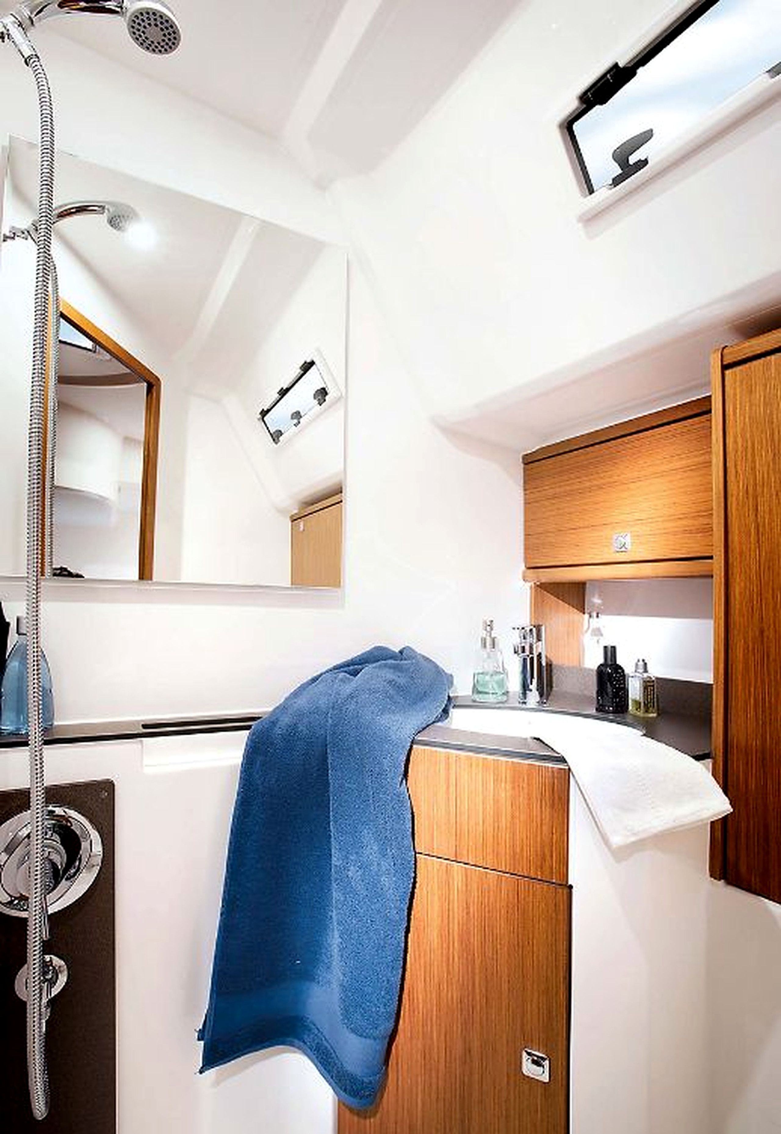 A compact bathroom with a shower, a mirror, a sink with a towel, and a wooden cabinet.