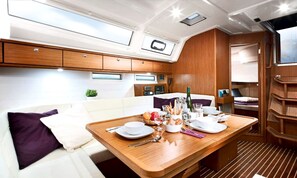 A compact, well-lit interior with a dining area, a small kitchenette, and a seating area with a cushioned bench. - Sun-Kissed Sailing Adventure in Islas Esporadas (Skiathos)