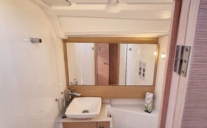 Un baño pequeño con lavamanos blanco, tocador de madera y espejo sobre el lavamanos.