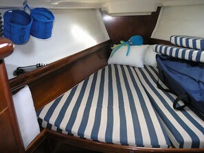 Ein kleines Boot Innere mit einem Einzelbett, gestreiften Kissen und zwei blauen Eimern.