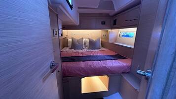 A compact, well-lit interior with a bunk bed, a small bedside table, and a control panel.