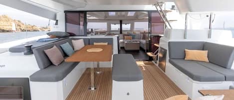 A modern boat interior with a dining area, seating, and a view of the water.