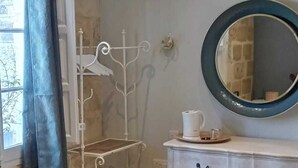 Quarto com um varal de metal, uma cômoda branca com gavetas, um espelho redondo e uma janela com cortina.