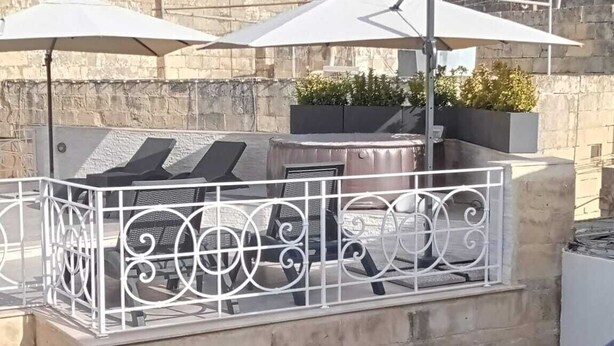 Terraço no telhado com mobiliário ao ar livre, um edifício de pedra e uma igreja ao fundo.