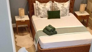 Quarto com cama, mesa de cabeceira, cadeira e pequena mesa.