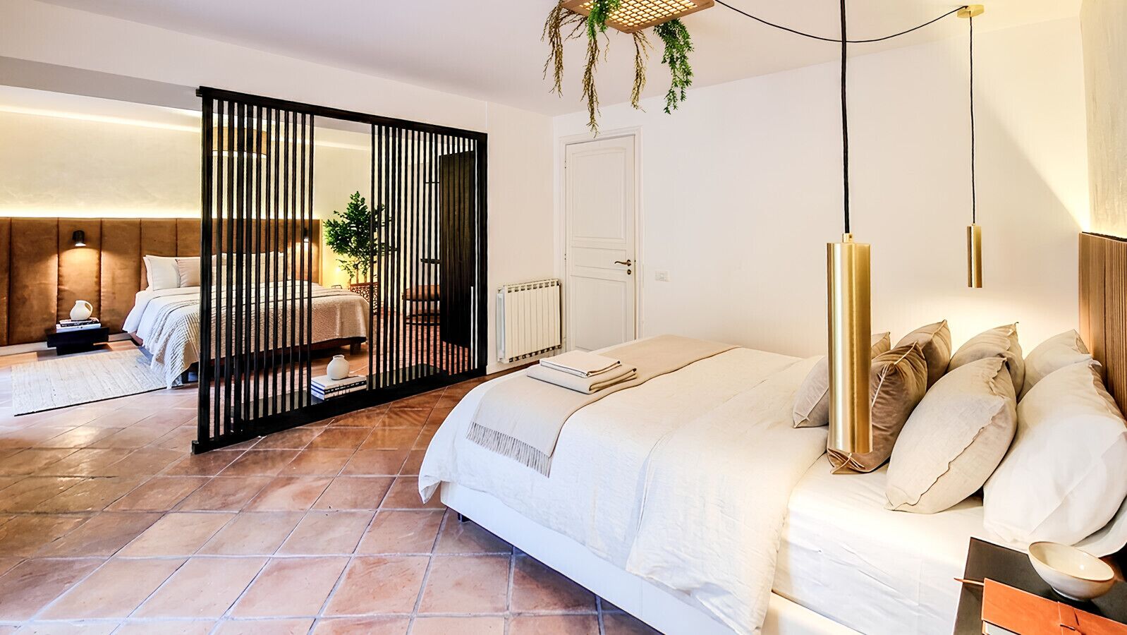 A hotel room with a bed, a desk, a chair, a radiator, and a door.