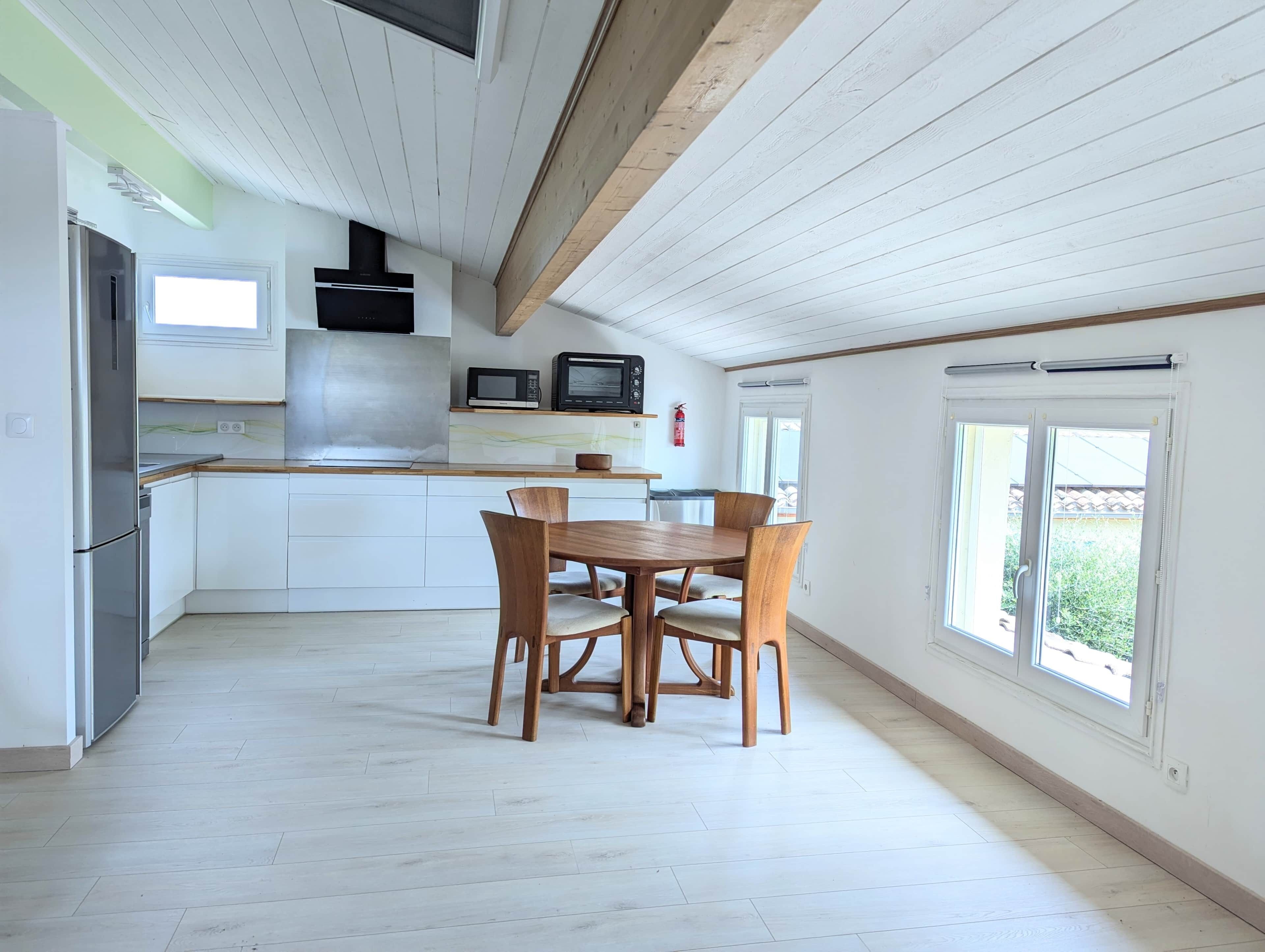 A modern kitchen with white cabinets, a dining table with chairs, and a view of the outdoors through large windows.