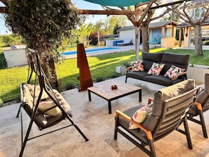 Eine Terrasse mit Gartenmöbeln, einem Schaukelstuhl und Blick auf Pool und Garten.