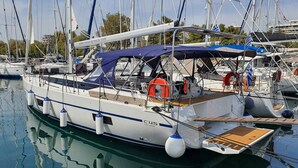 Un'imbarcazione a vela ormeggiata in una marina, con una copertura sul ponte, boe di salvataggio e un ponte in legno.
