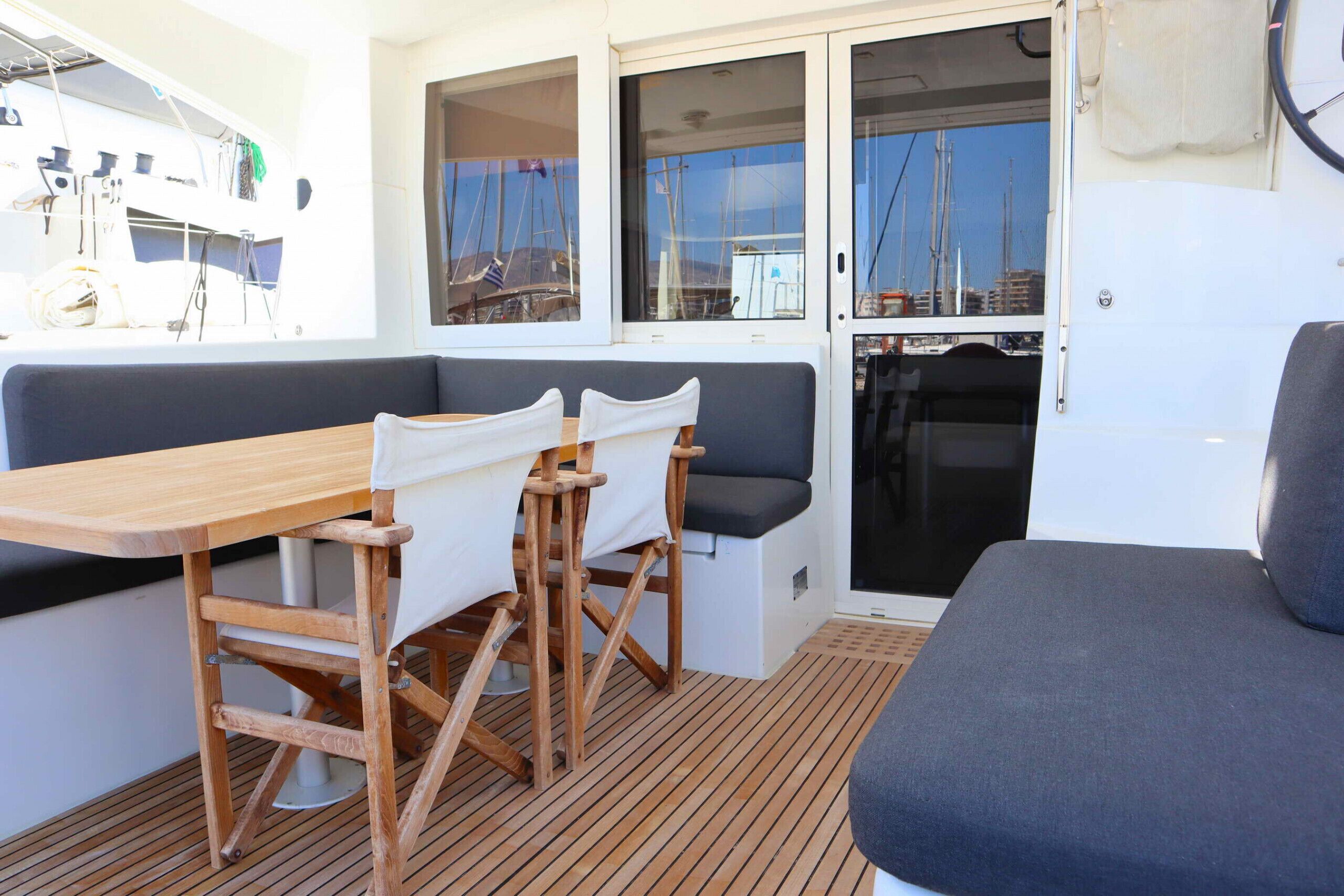 A dining area with a wooden table and chairs, a cushioned bench, and a view of the sea through large windows.