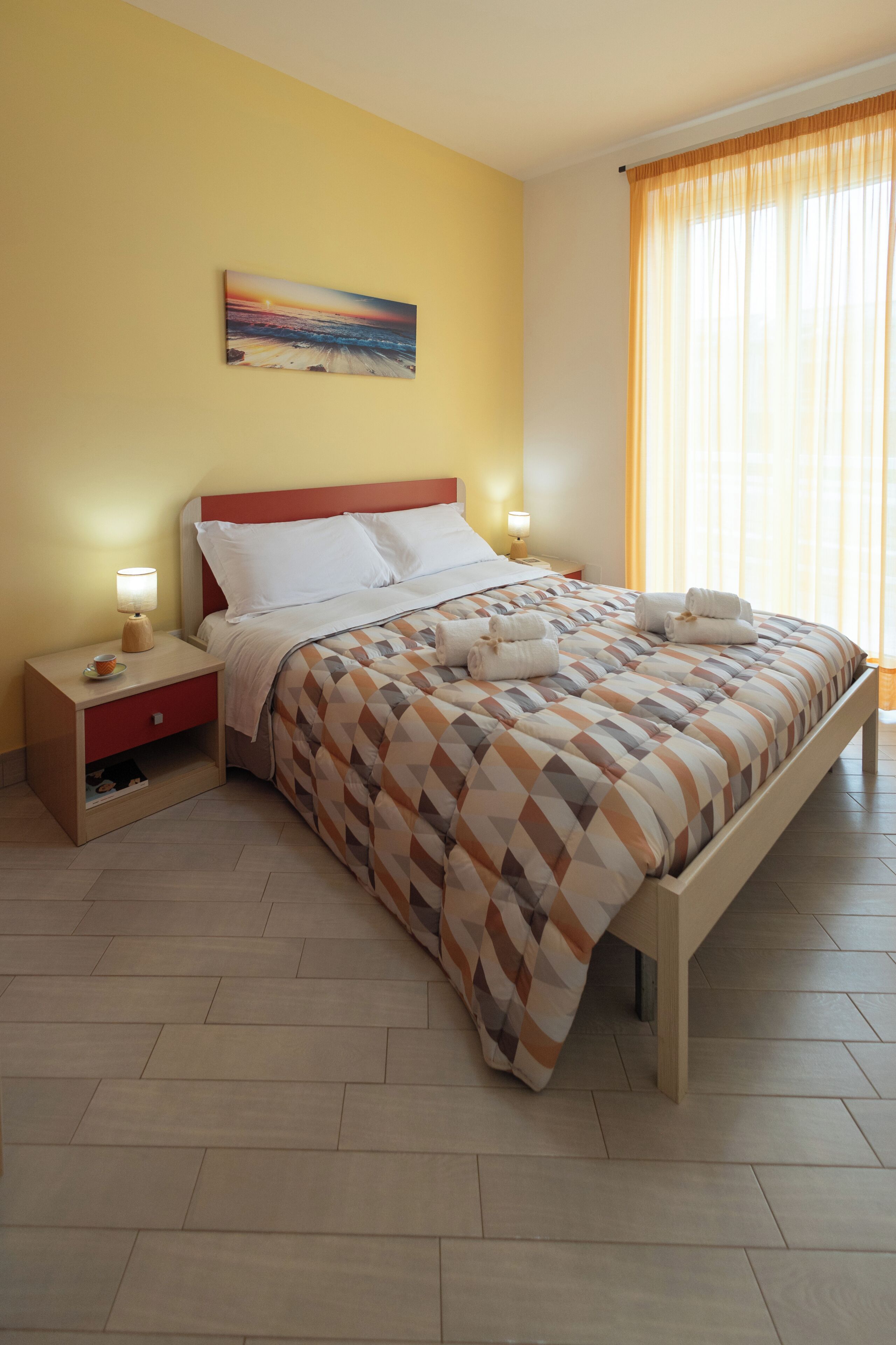 Un lit bien fait, recouvert d’une couvre-lit à motifs, une table de chevet avec une lampe et un tableau accroché au mur.