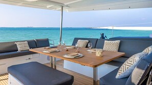 A dining area with a table set for two, a cushioned seating area, and a view of the sea. - Caribbean Dream: Sun-soaked Sailing Adventure from Tortola, Islas Vírgenes Británicas (Road Town)