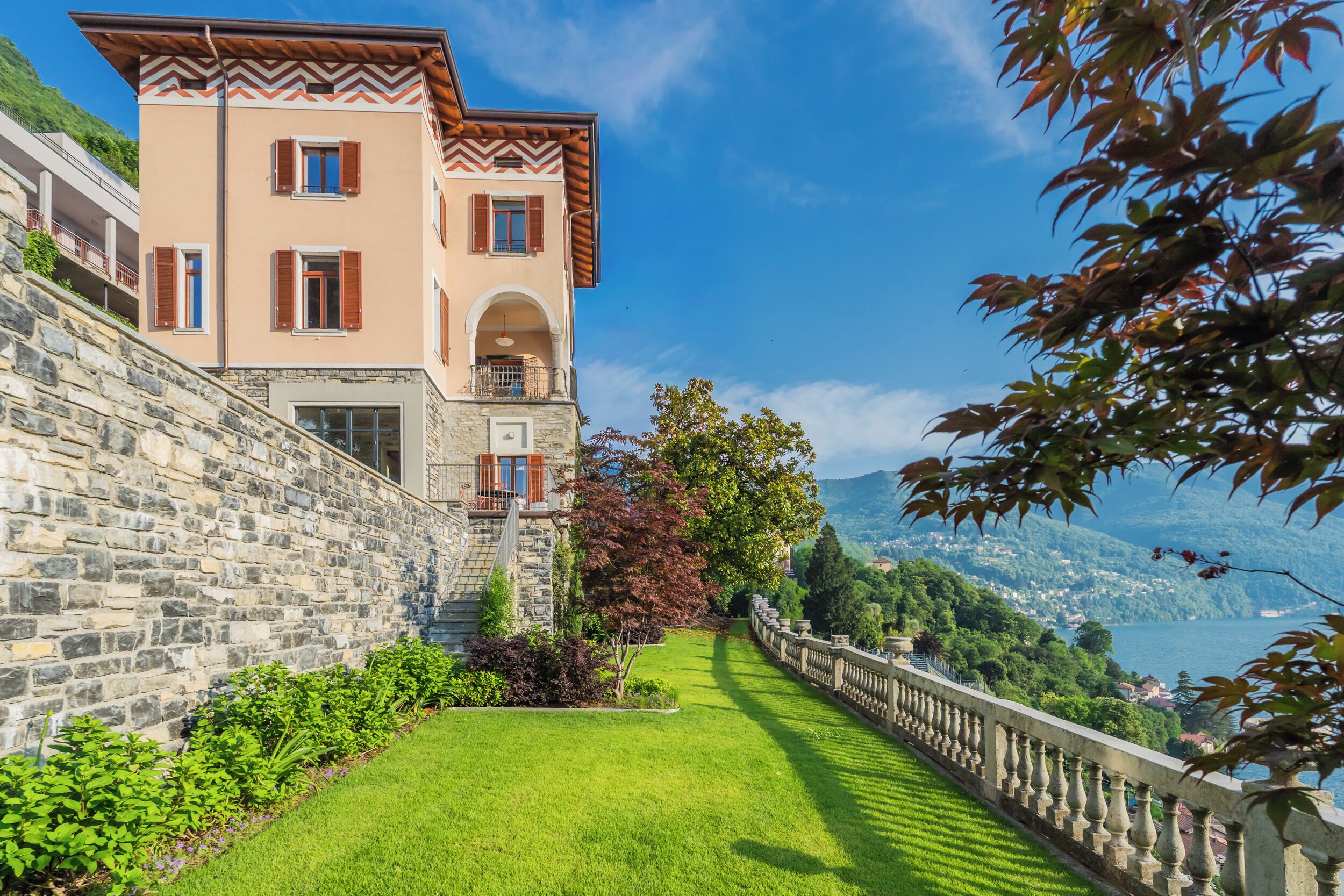 Un bâtiment en pierre doté d’un balcon, d’une pelouse bien entretenue et offrant une vue sur un lac.