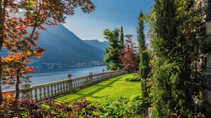 A garden with a water body, mountains, and a stone wall. - Villa Madonnina (Pognana Lario)
