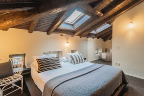Una camera da letto con un velux, un letto con cuscini, una sedia e un bagno piccolo.