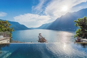 A clear view of a lake with mountains in the background, a wooden deck, and a small tree in the water. - Villa Madonnina (Pognana Lario)