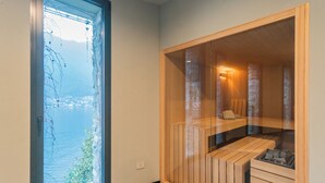 A modern room with a large window, a wooden bench, and a small seating area. - Villa Madonnina (Pognana Lario)
