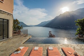 Una piscina a sfioro con sedie a sdraio, un solarium in pietra e vista sulle montagne.